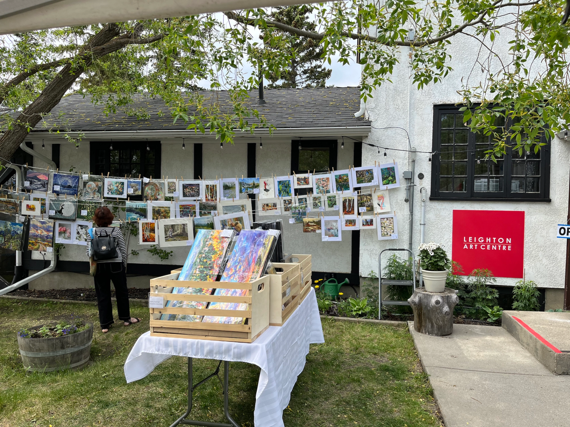 Outdoor art market with a person viewing artworks displayed on a building and a table.