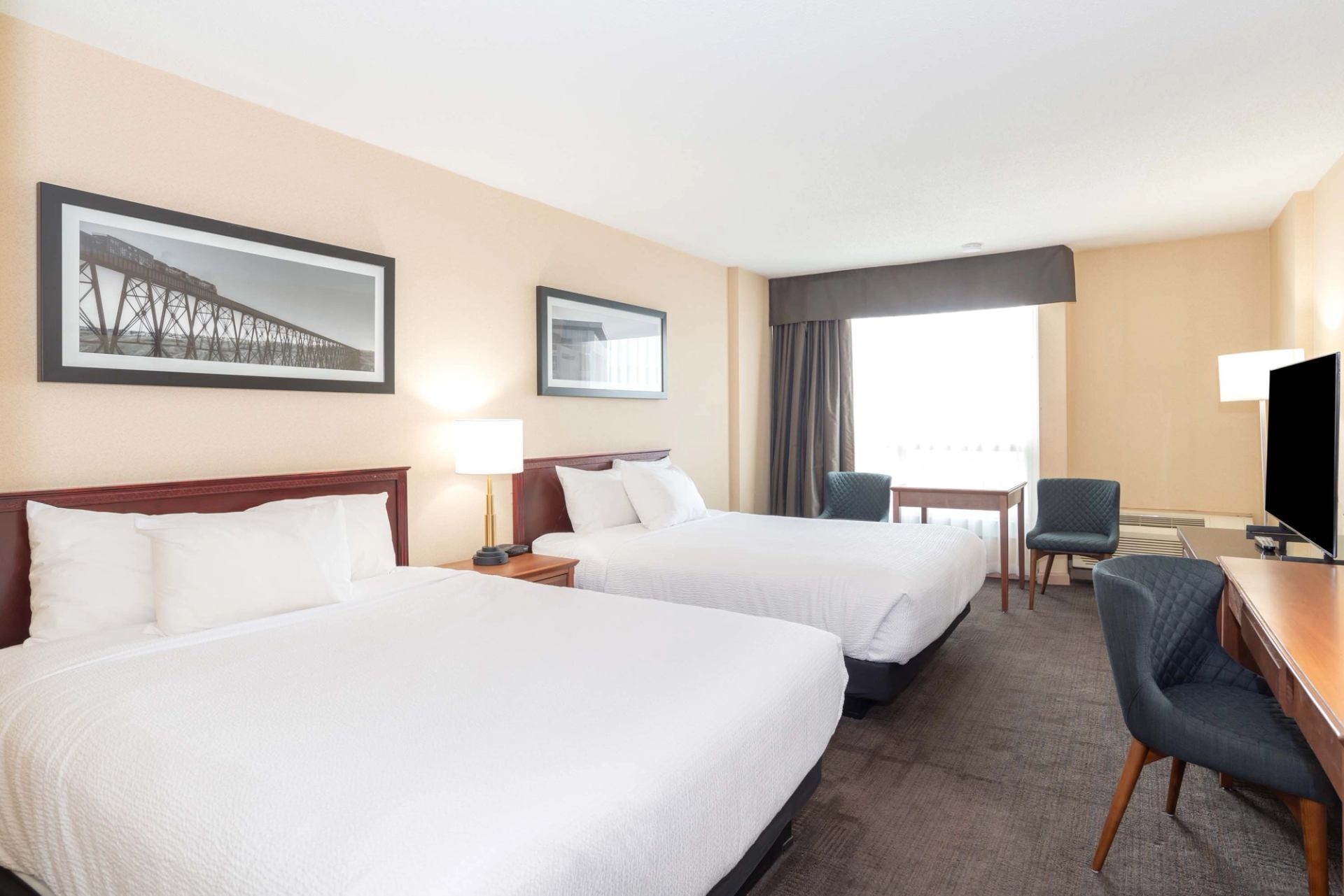 A hotel room with two beds, desk, chairs, and window seating area.