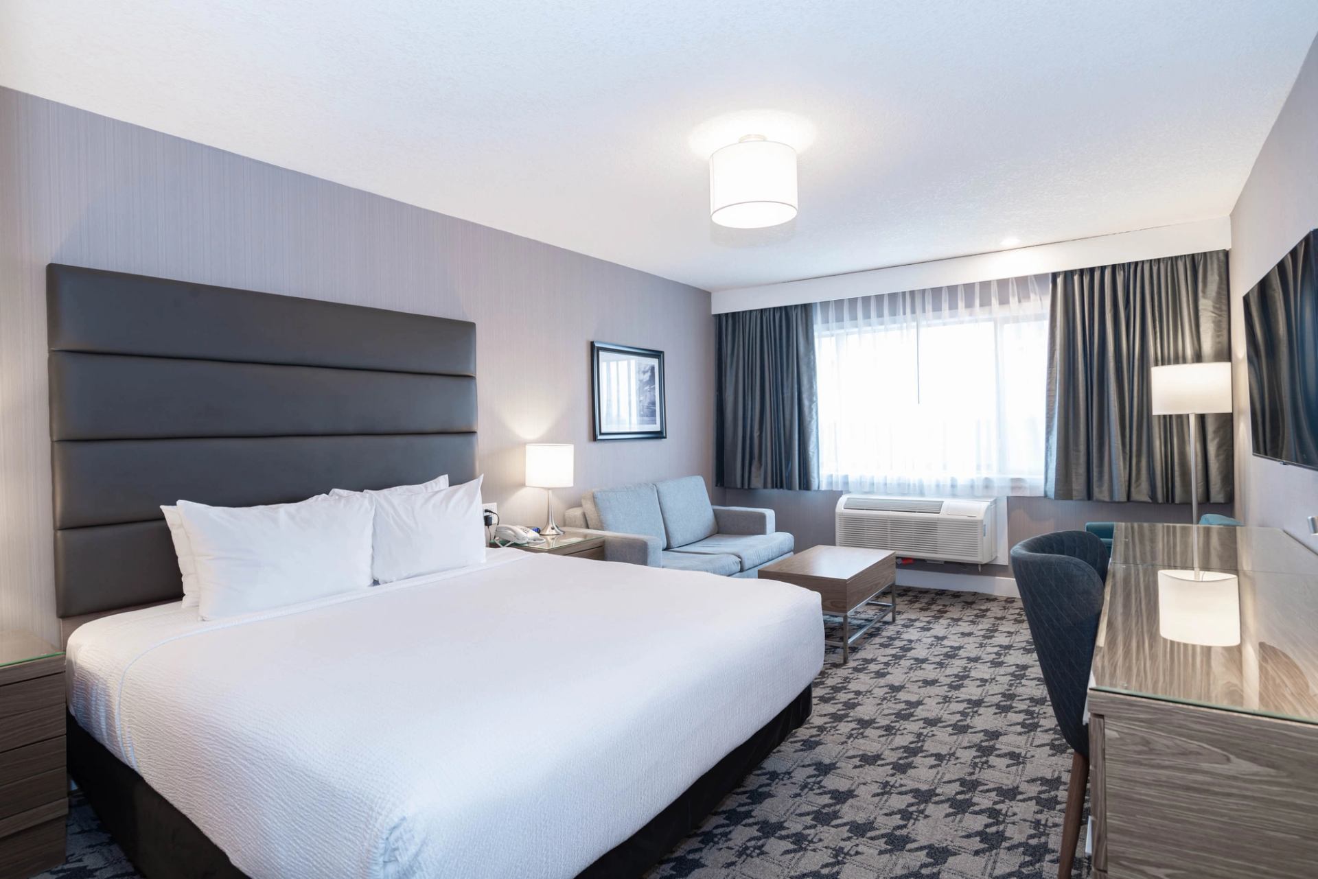 Hotel room with king bed, sofa, desk, and large window.