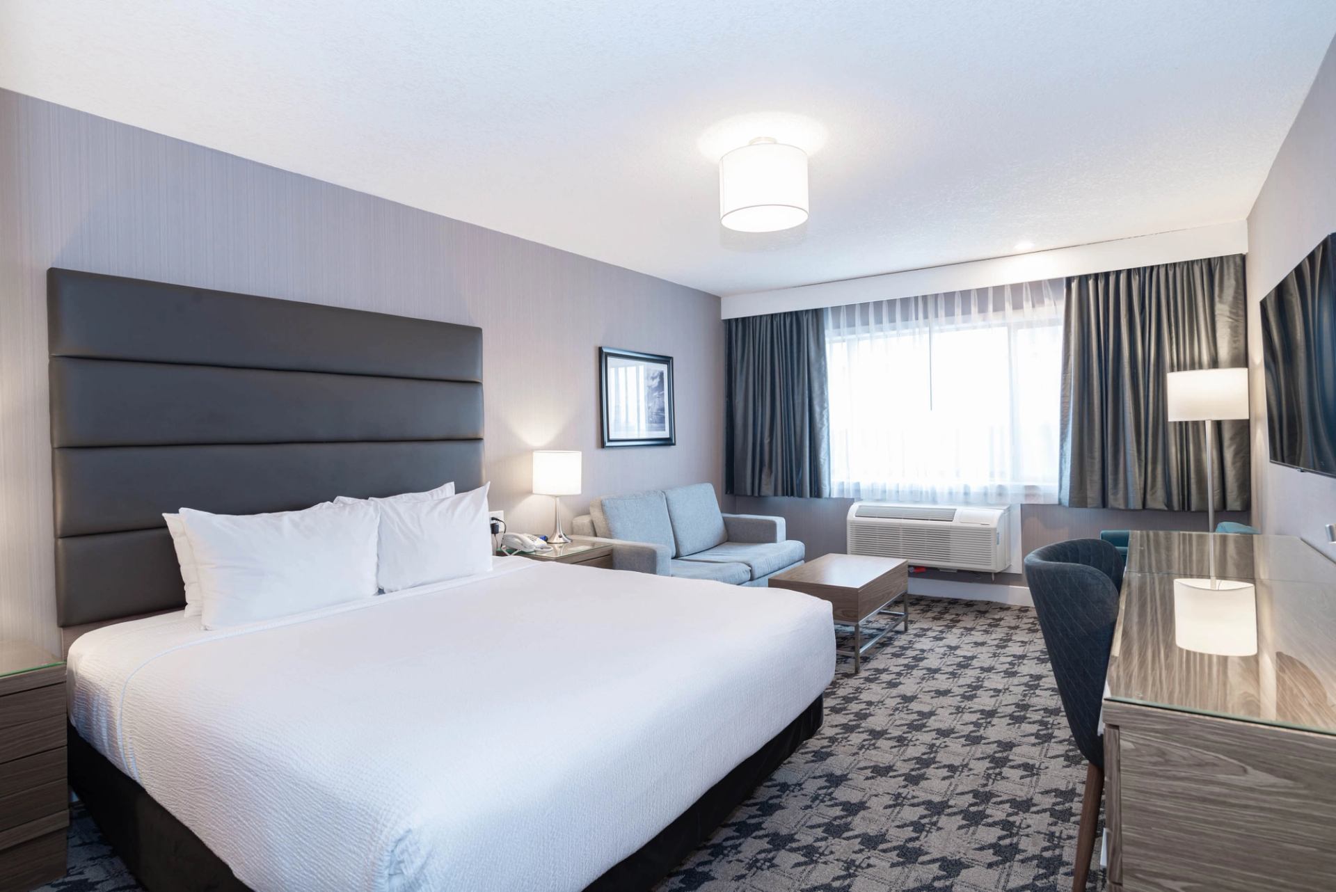 Hotel room with king bed, sofa, desk, and large window.