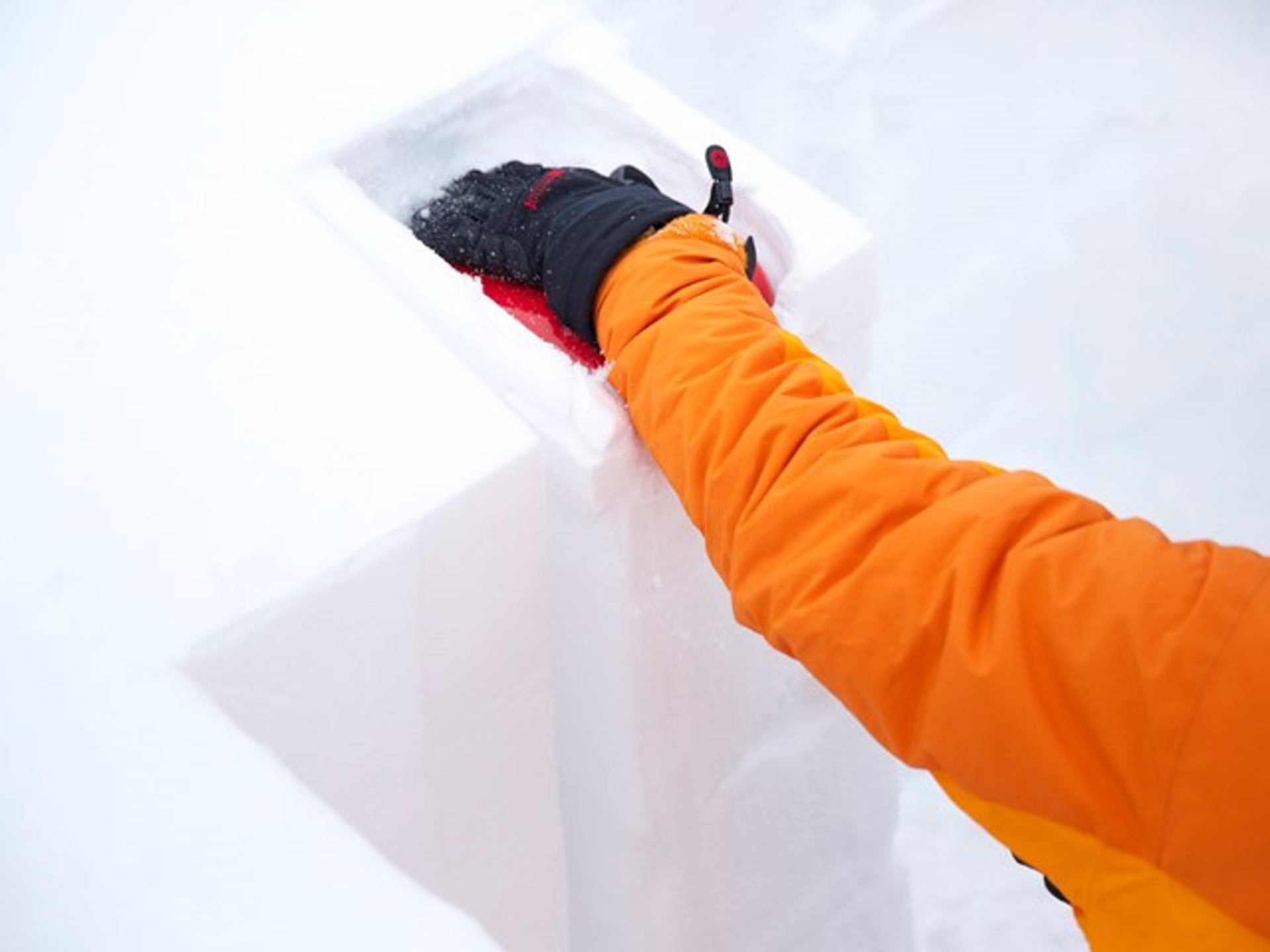 Gloved hand performing a snow stability test by cutting a block from a snow pit.