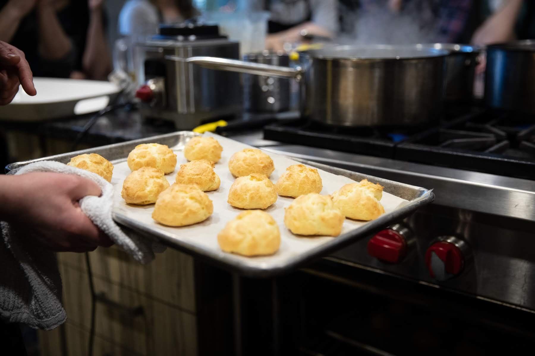 Tray of baked biscuit dough rounds on a metal pan at an industrial kitchen station.