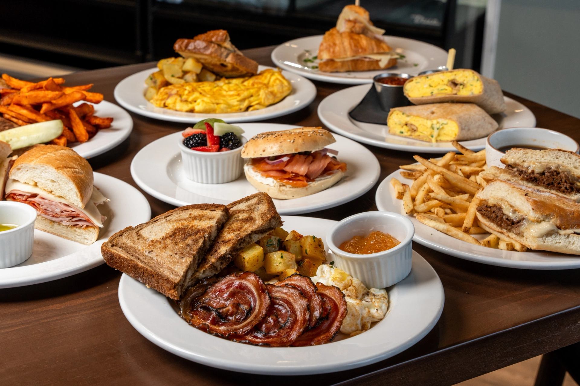 A variety of plated sandwiches, breakfast dishes, fries, and pastries on a table.