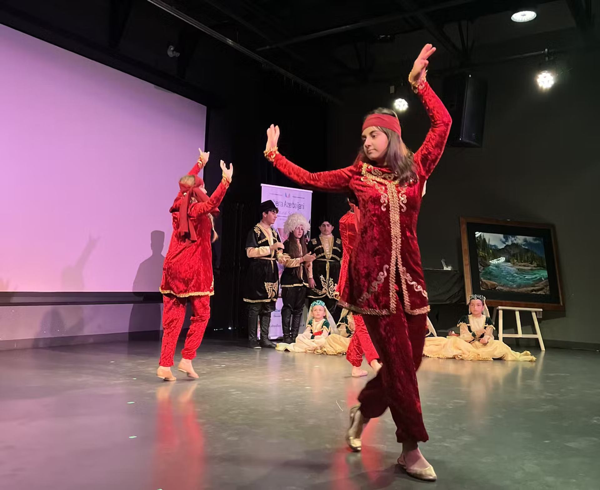 Performers in traditional red costumes dance on stage during a cultural celebration.