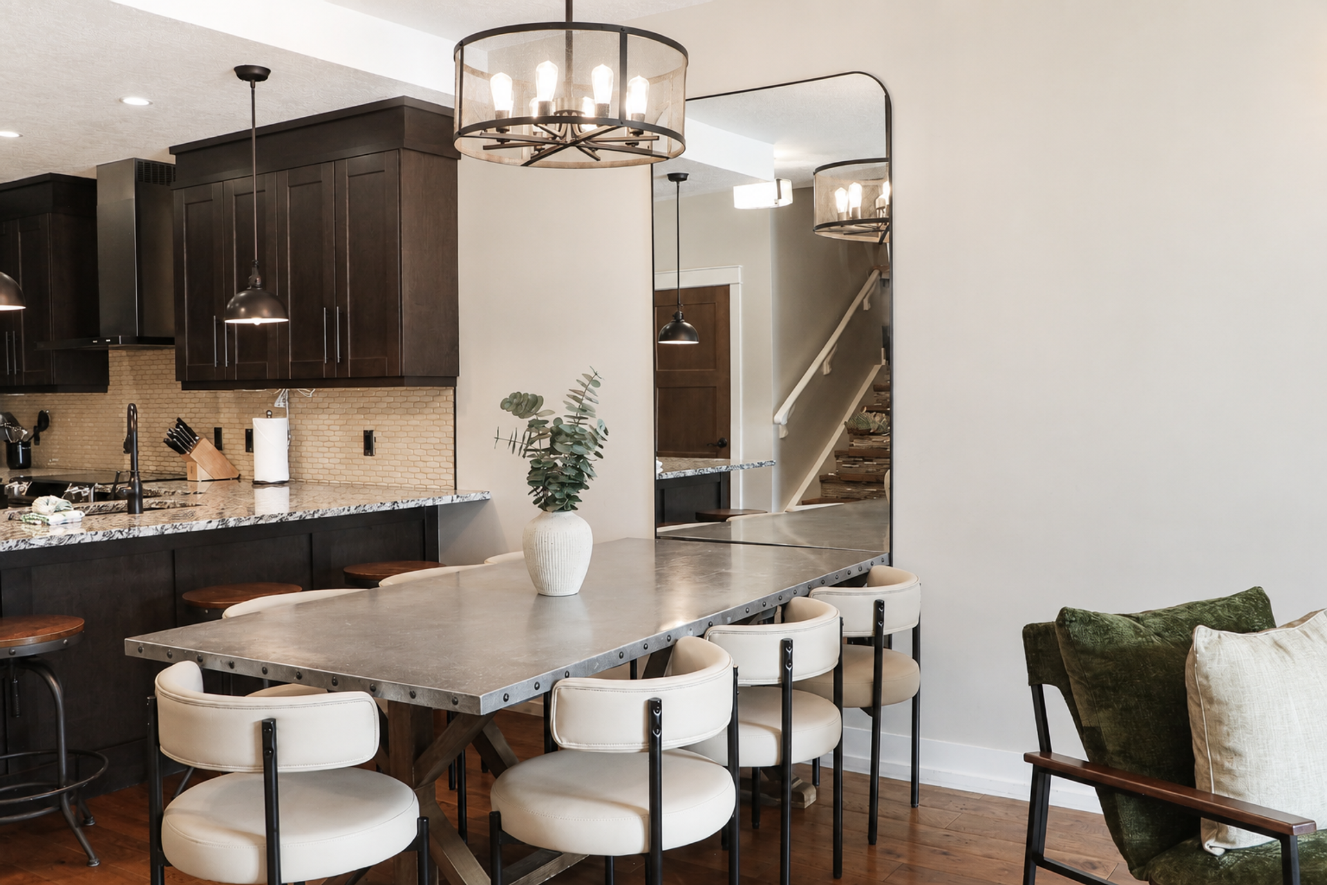 Dining table and chairs beside a dark-cabinet kitchen with pendant lighting.