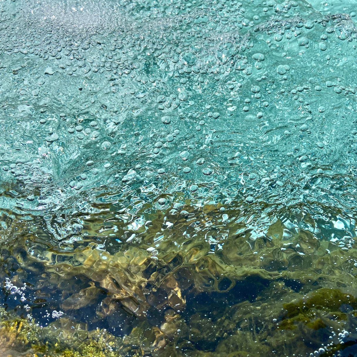 Clear turquoise river water with bubbles and rocks visible beneath the surface.