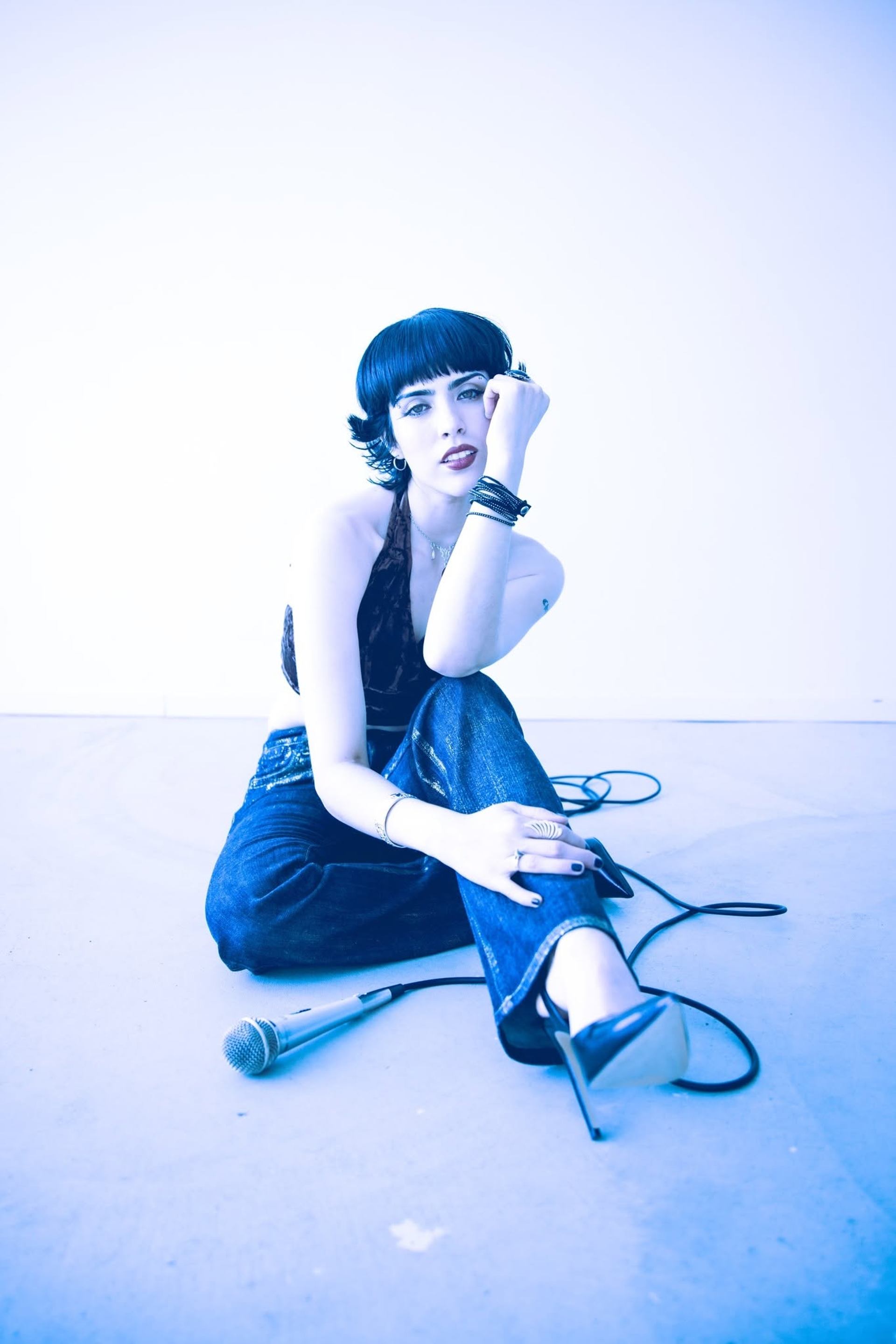 Person with short dark hair sits beside a wired microphone under blue lighting.