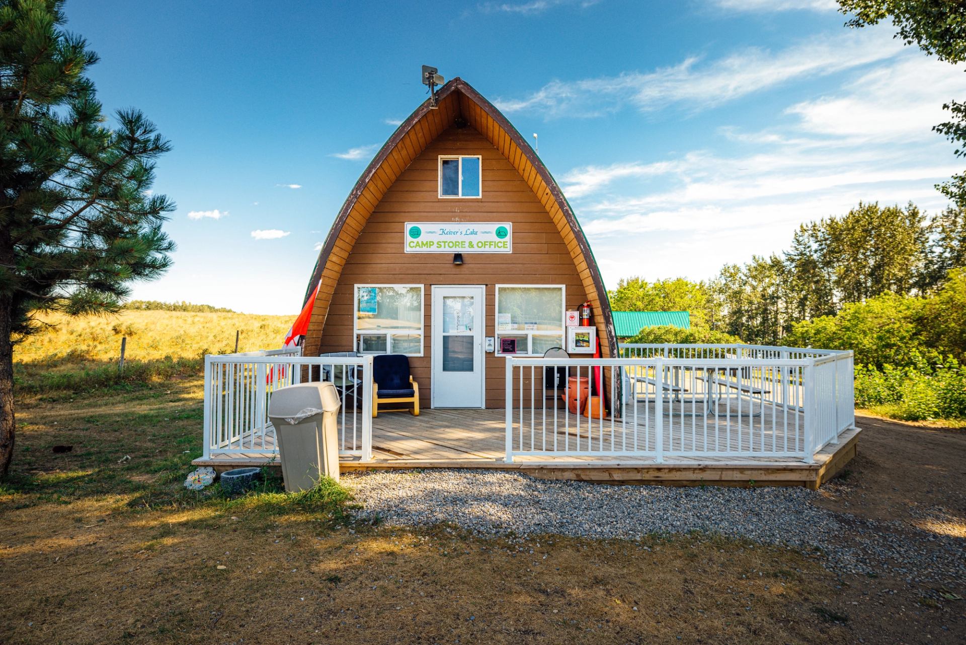 A small camp store and office with an A-frame roof, surrounded by trees and open fields.
