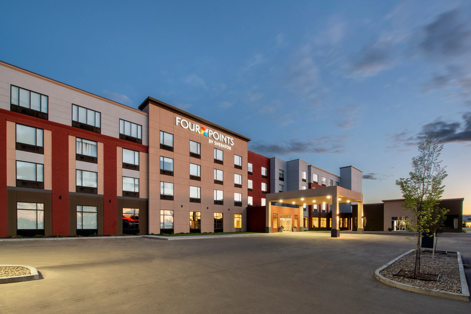 Four Points by Sheraton Grande Prairie hotel exterior with entrance canopy under blue sky.