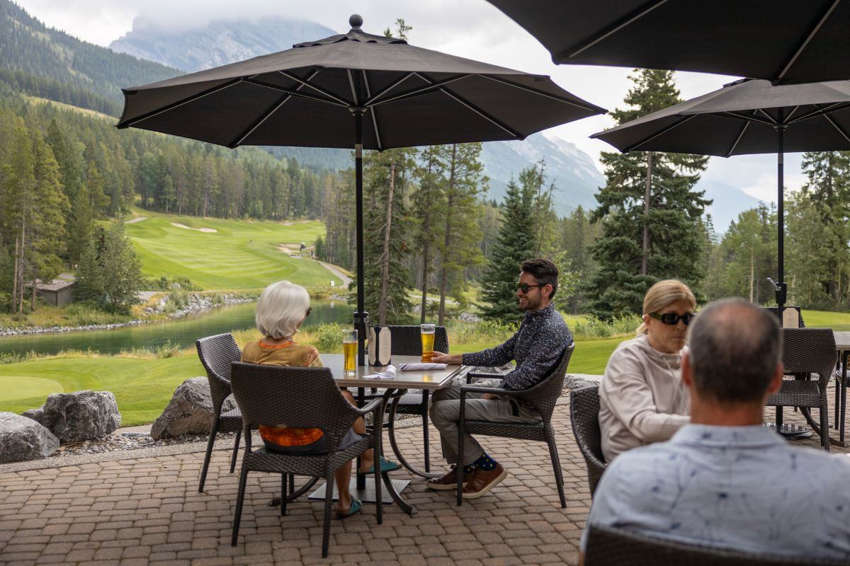 Outdoor patio dining with umbrellas overlooking a scenic golf course and forested mountains.
