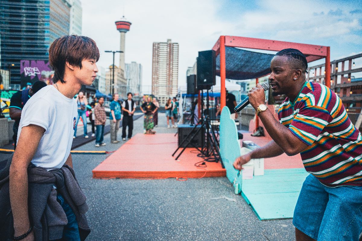 People gather at an outdoor event near a stage, with Calgary Tower visible in the background