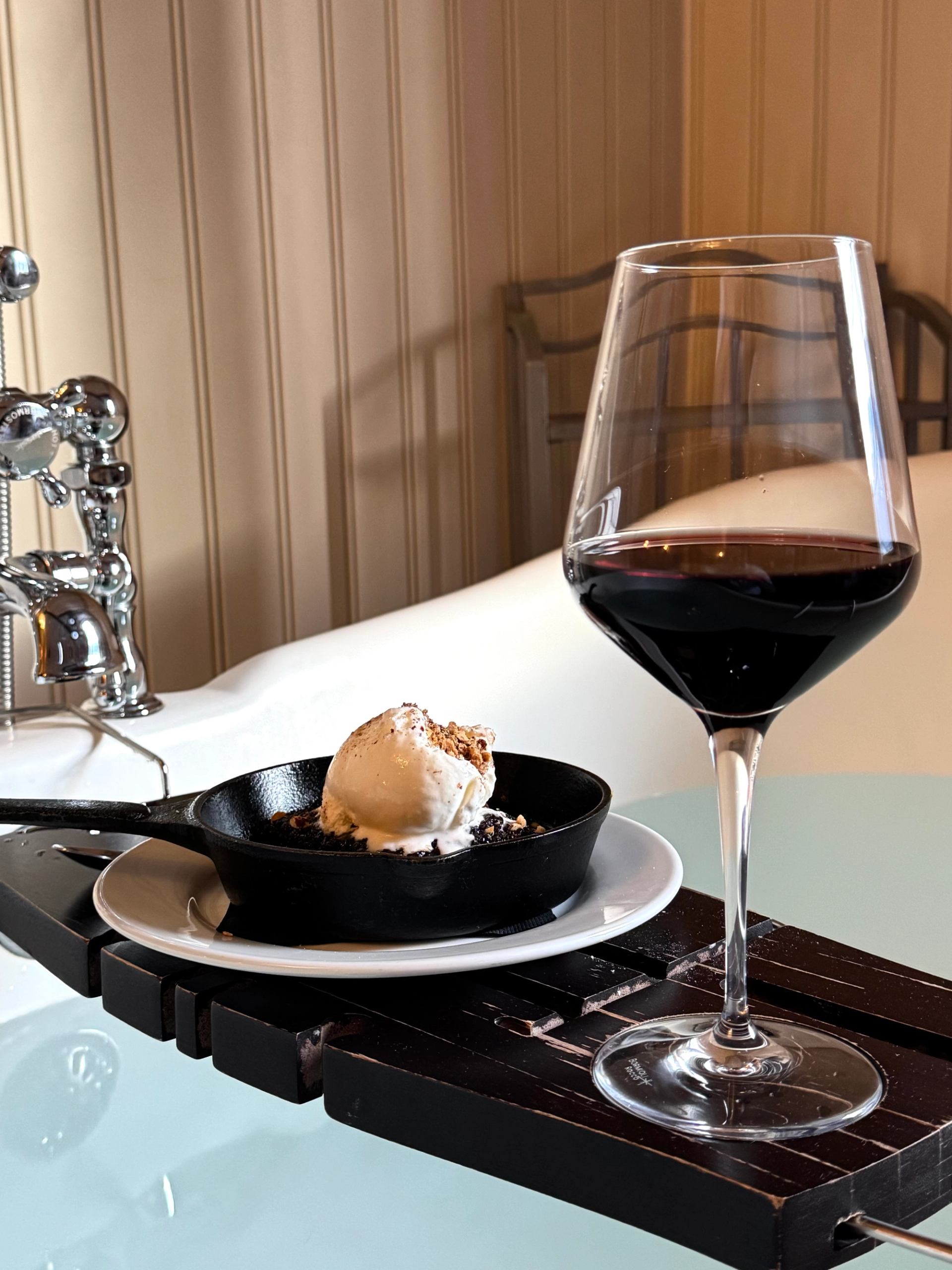 Dessert and wine served by a bathtub in a cozy, luxurious setting.