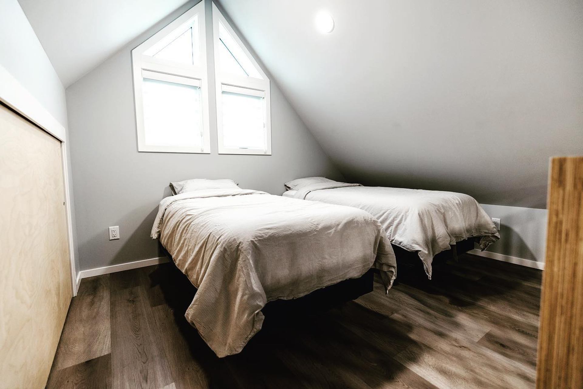 Loft room with two twin beds under a sloped ceiling and a bright triangular window.