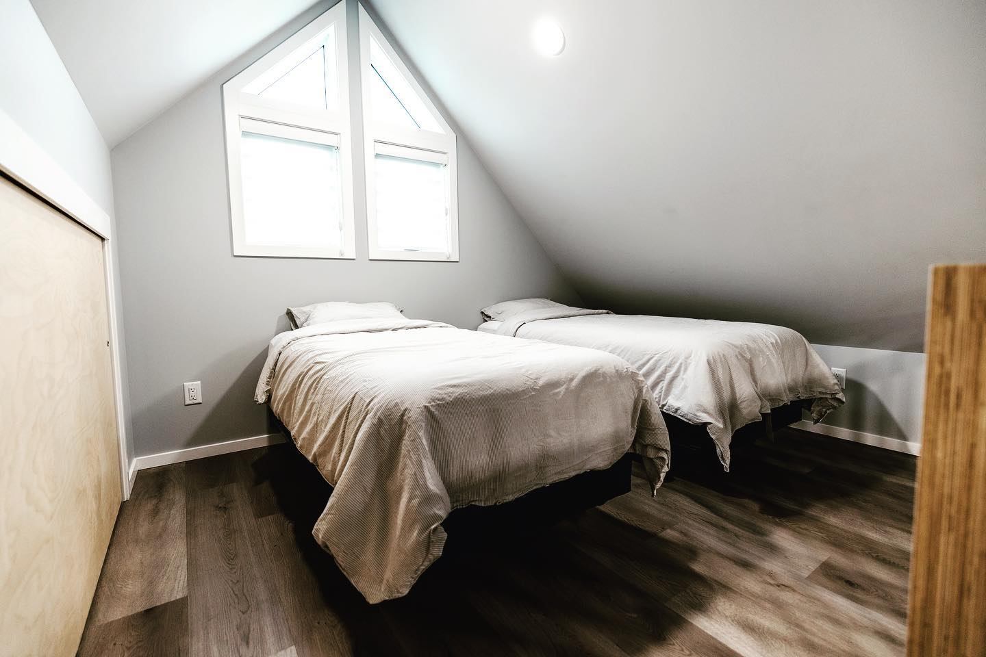 Loft room with two twin beds under a sloped ceiling and a bright triangular window.
