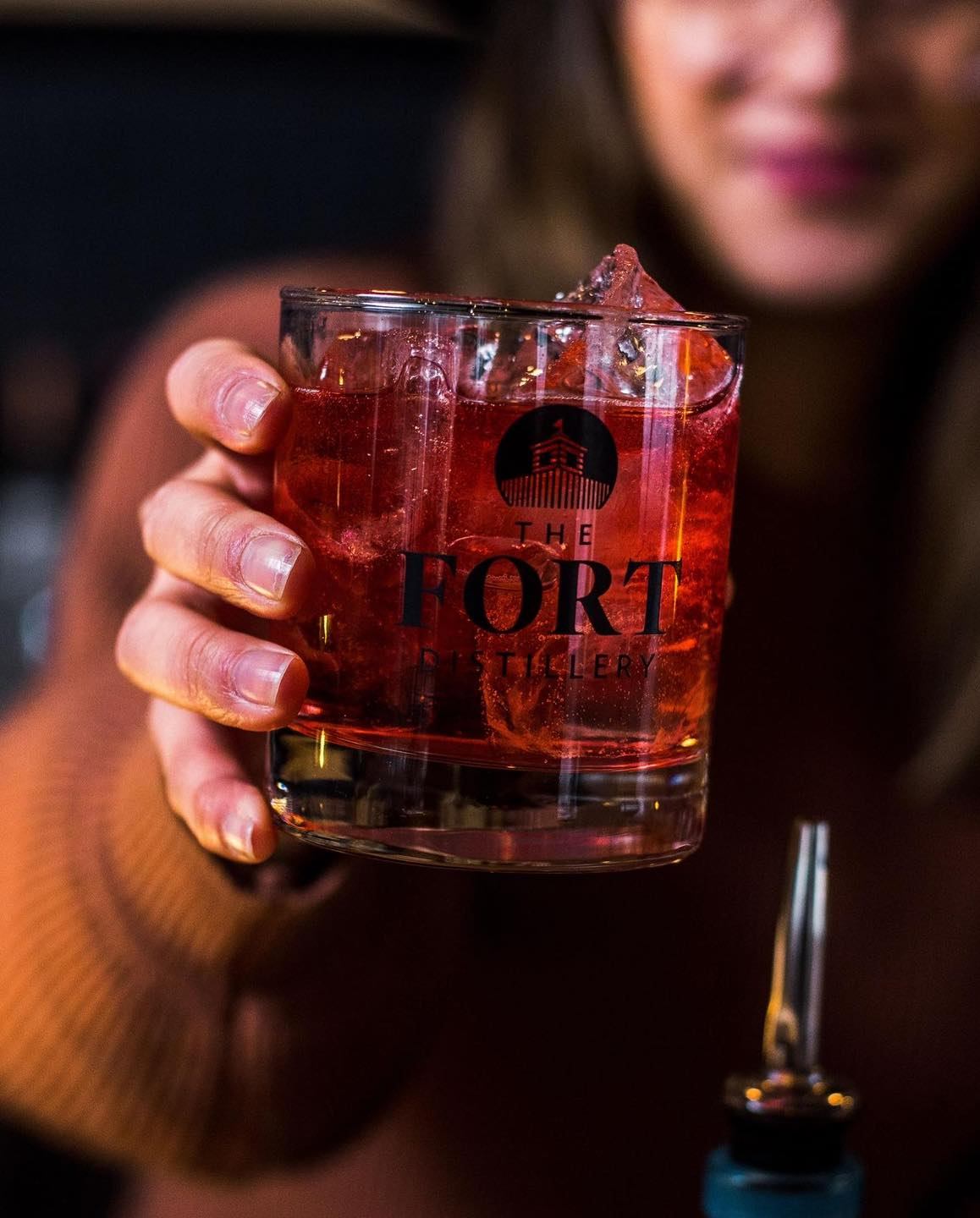 Red cocktail in a Fort Distillery glass held above the bar