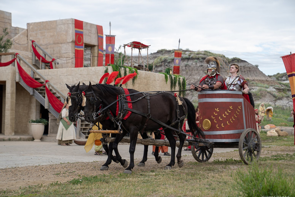 A chariot driven by Roman soldiers and led by two black horses on the set.