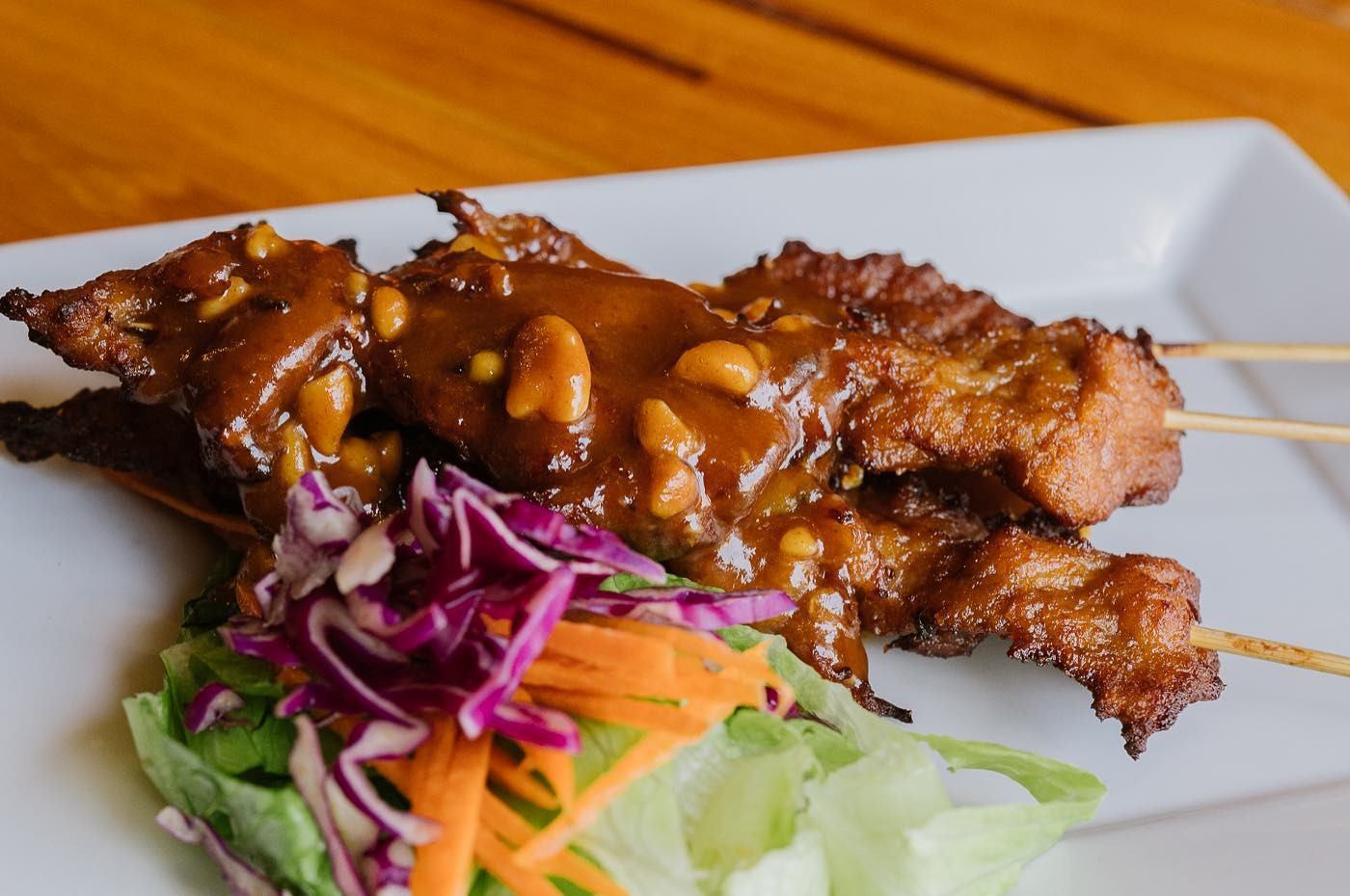 Grilled skewers with peanut sauce and fresh vegetables on a white plate.