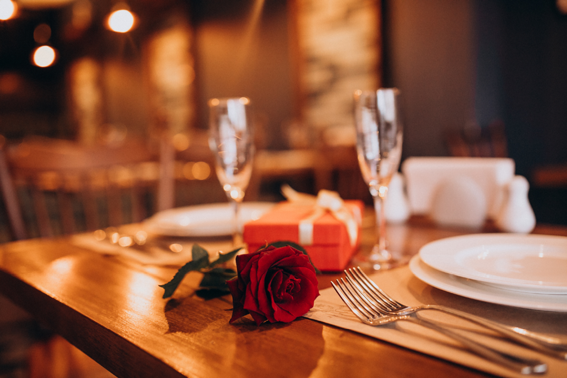 Romantic table setting with champagne glasses, a red rose, and a gift for Valentine’s Dinner.