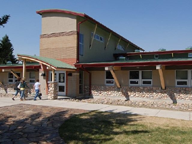 Modern visitor center with green roof, brick walls, and people walking toward entrance.