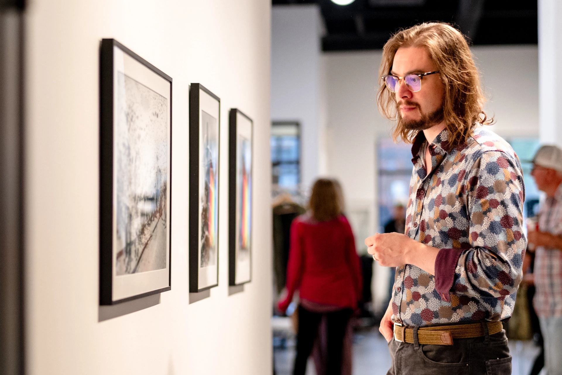 A man looks at a series of artworks mounted on a wall in a gallery.