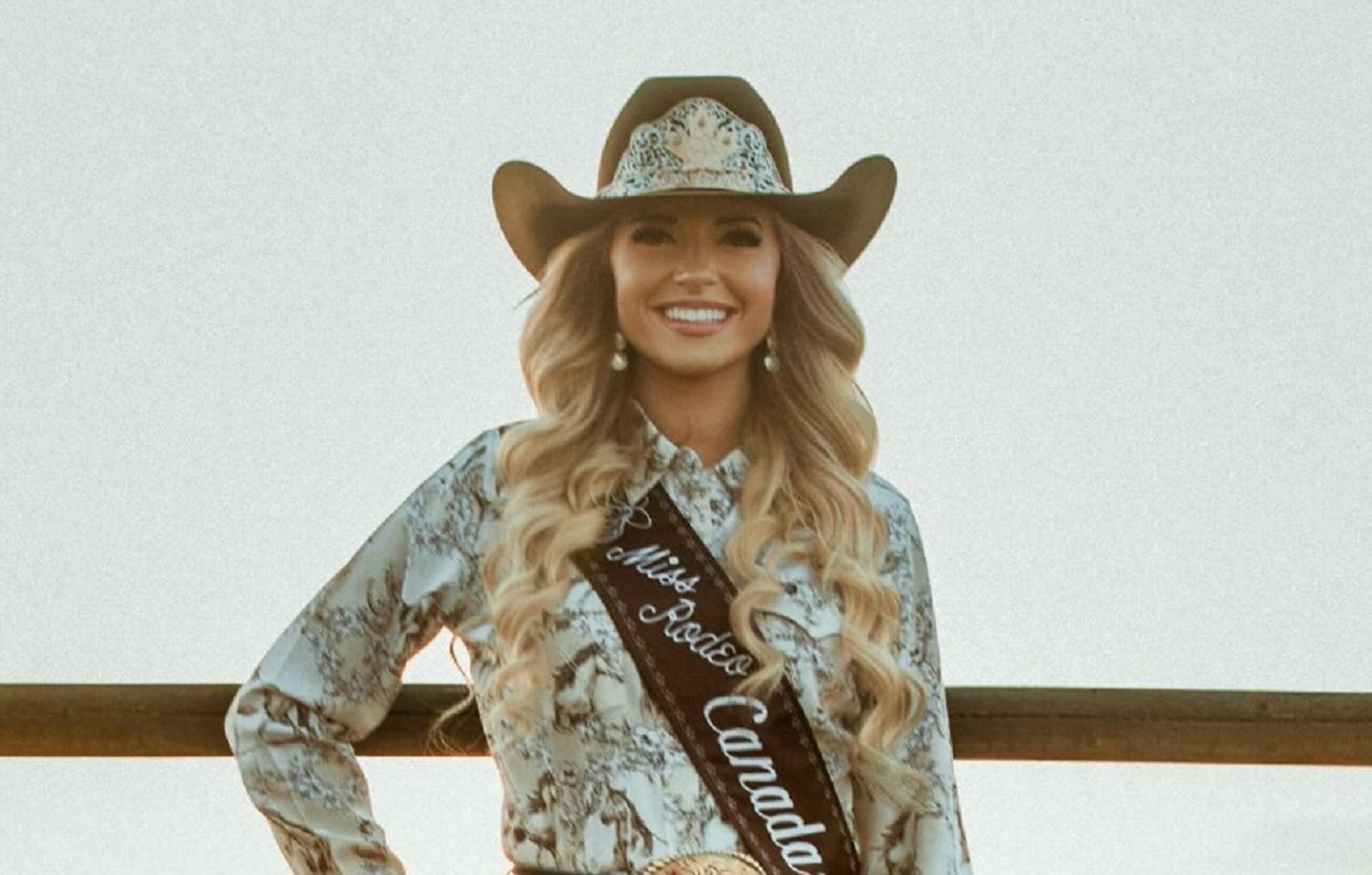 Rodeo queen in cowboy hat and sash reading Miss Rodeo Canada stands by wooden fence