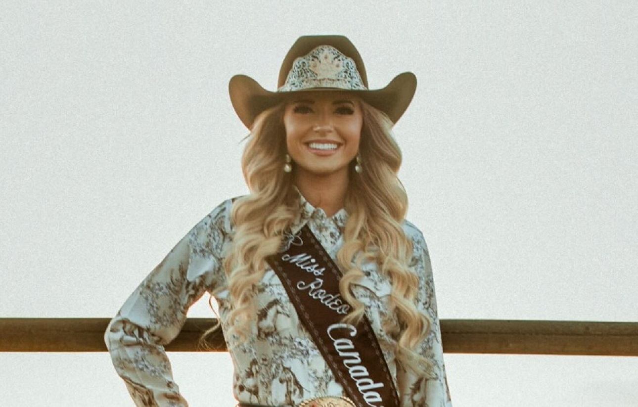 Rodeo queen in cowboy hat and sash reading Miss Rodeo Canada stands by wooden fence