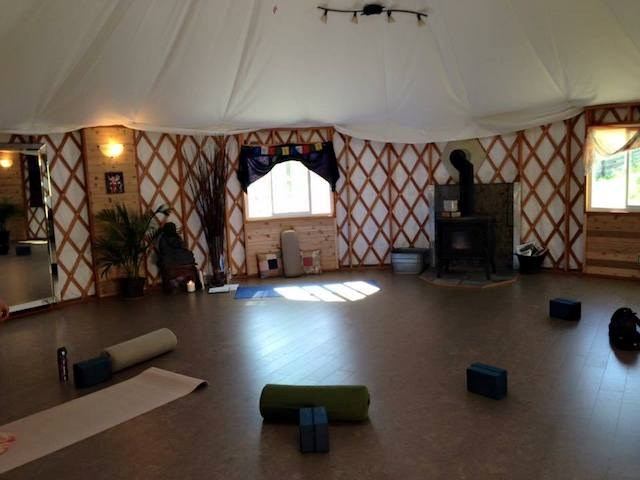 Yurt interior with yoga mats and blocks on floor, wood stove and windows.