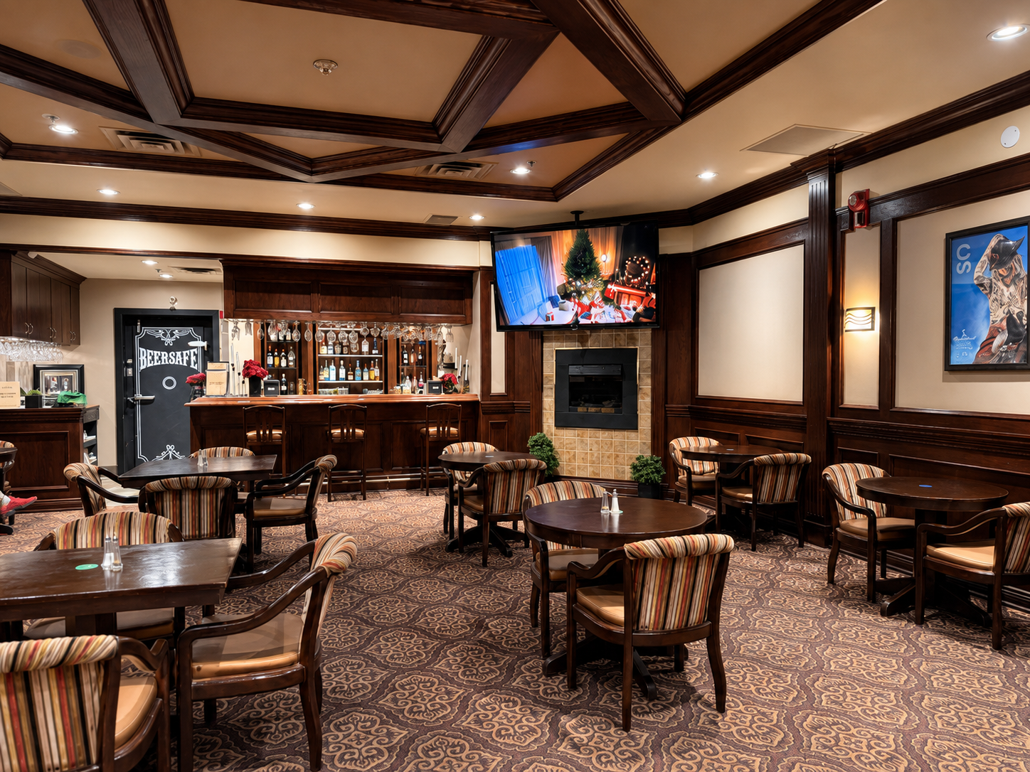 Hotel lounge bar with round tables, striped chairs and television above fireplace.