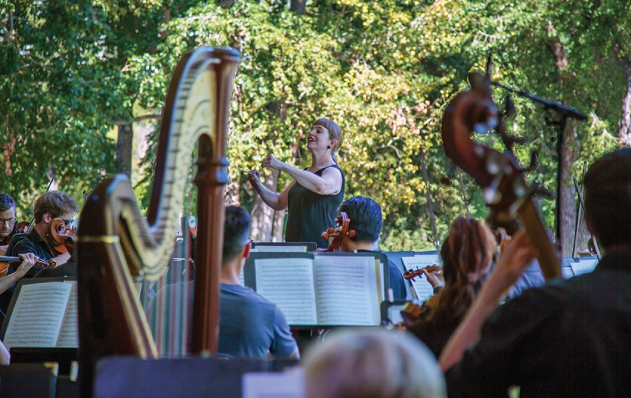 Outdoor orchestra with conductor and musicians performing among trees at Phil in the Park.