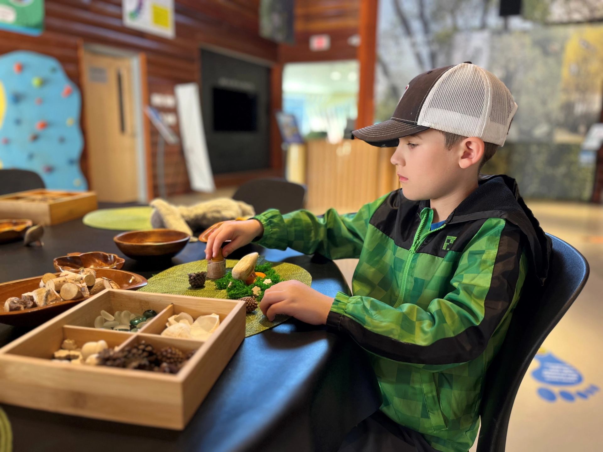 A child arranges natural materials like stones and wood pieces at a play table.