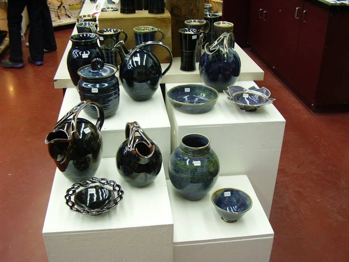 Glazed ceramic bowls, vases, and pitchers are arranged on white display stands inside a pottery stud