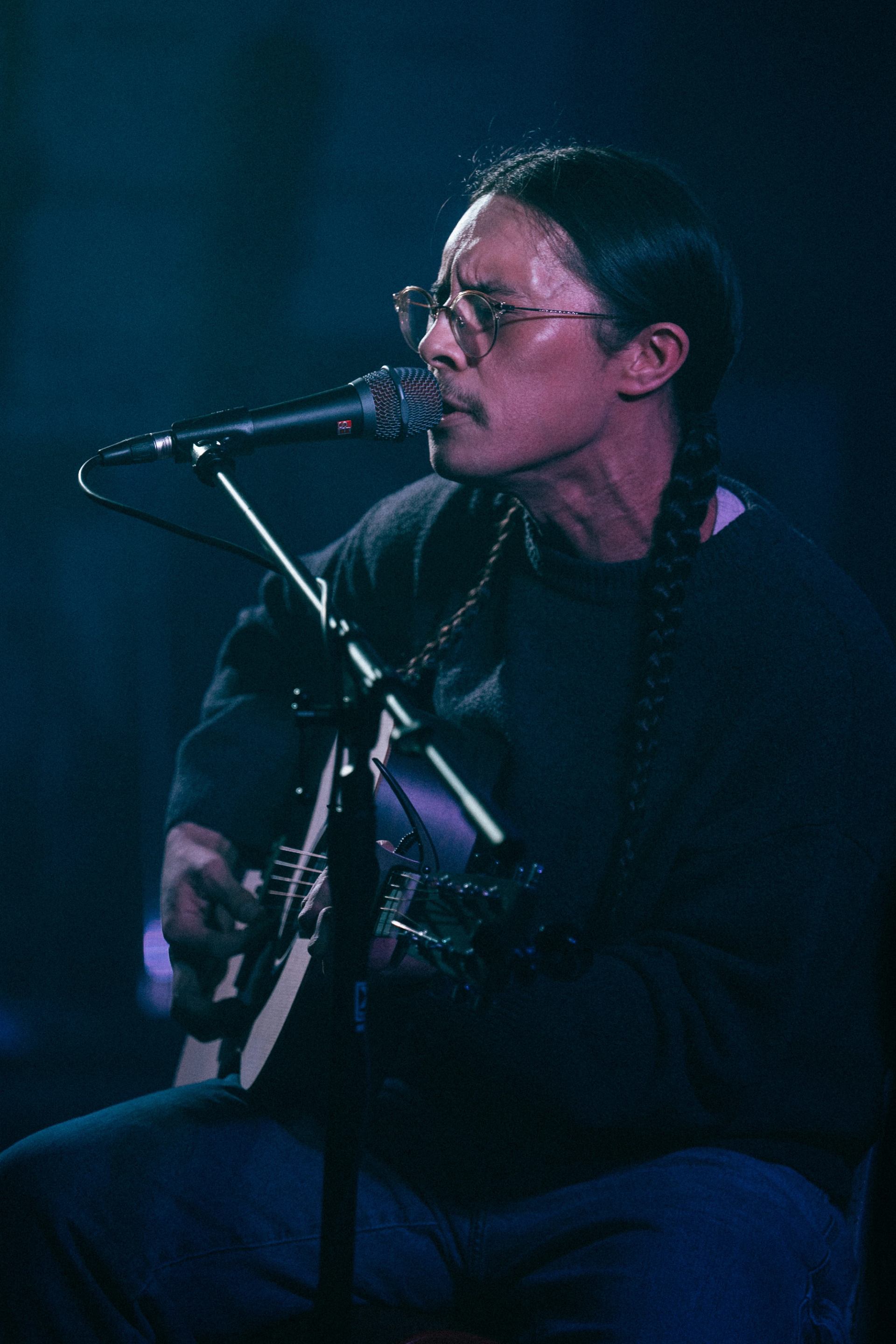 Musician performing on stage with an acoustic guitar under blue stage lighting