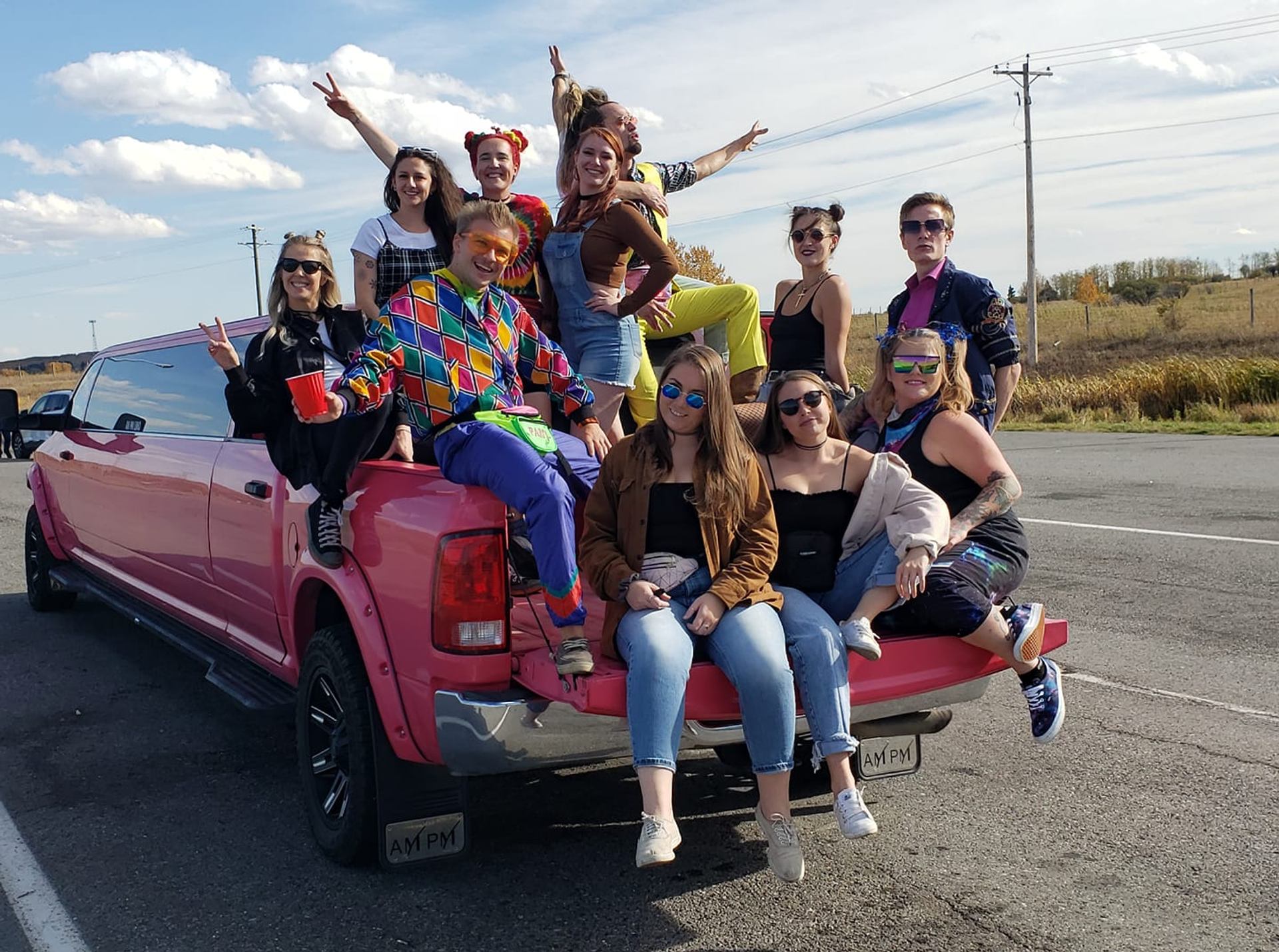 Group celebrating on a pink truck with festive outfits and open-road backdrop.