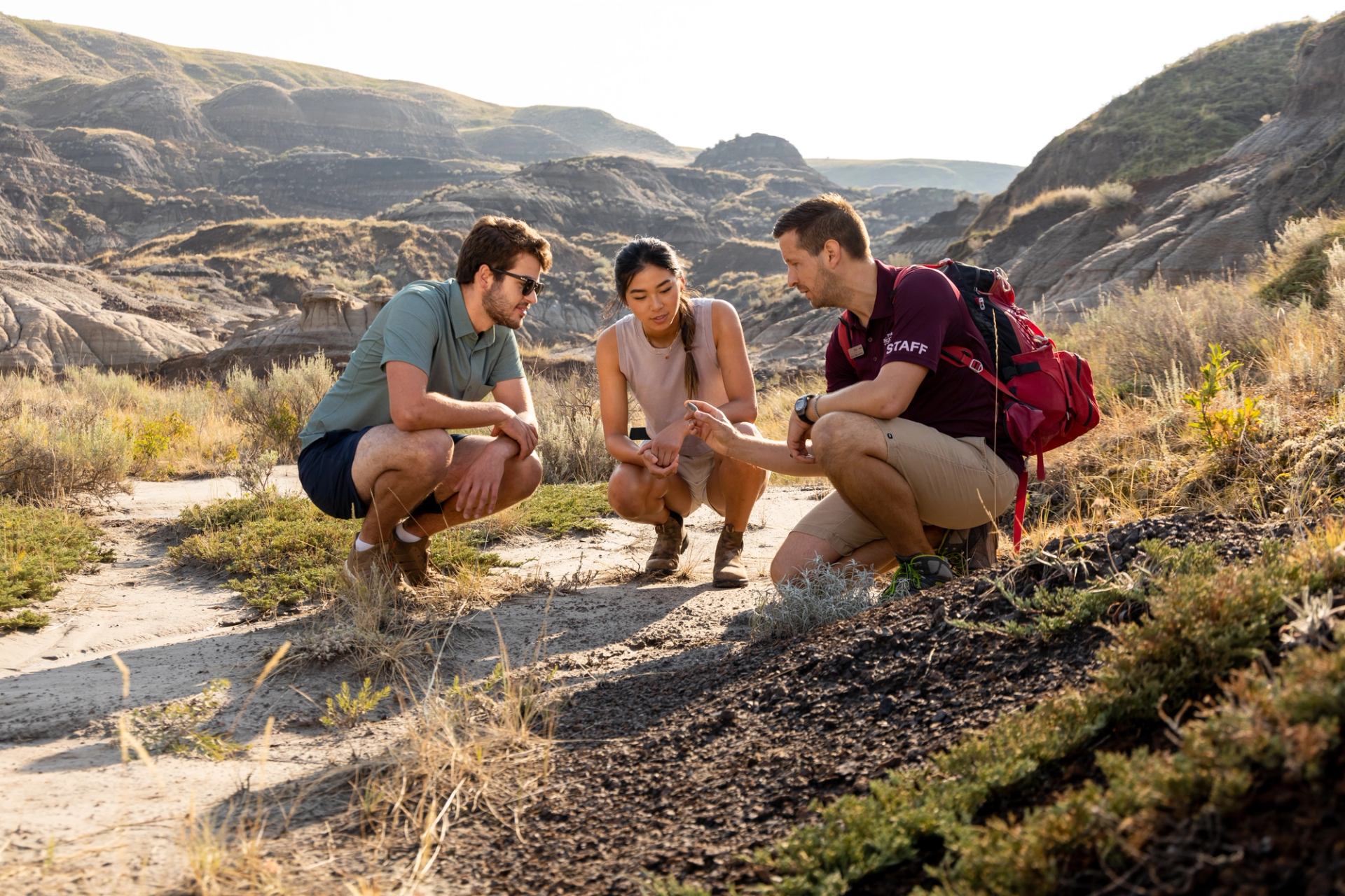 Three people crouched in rocky terrain, observing nature.