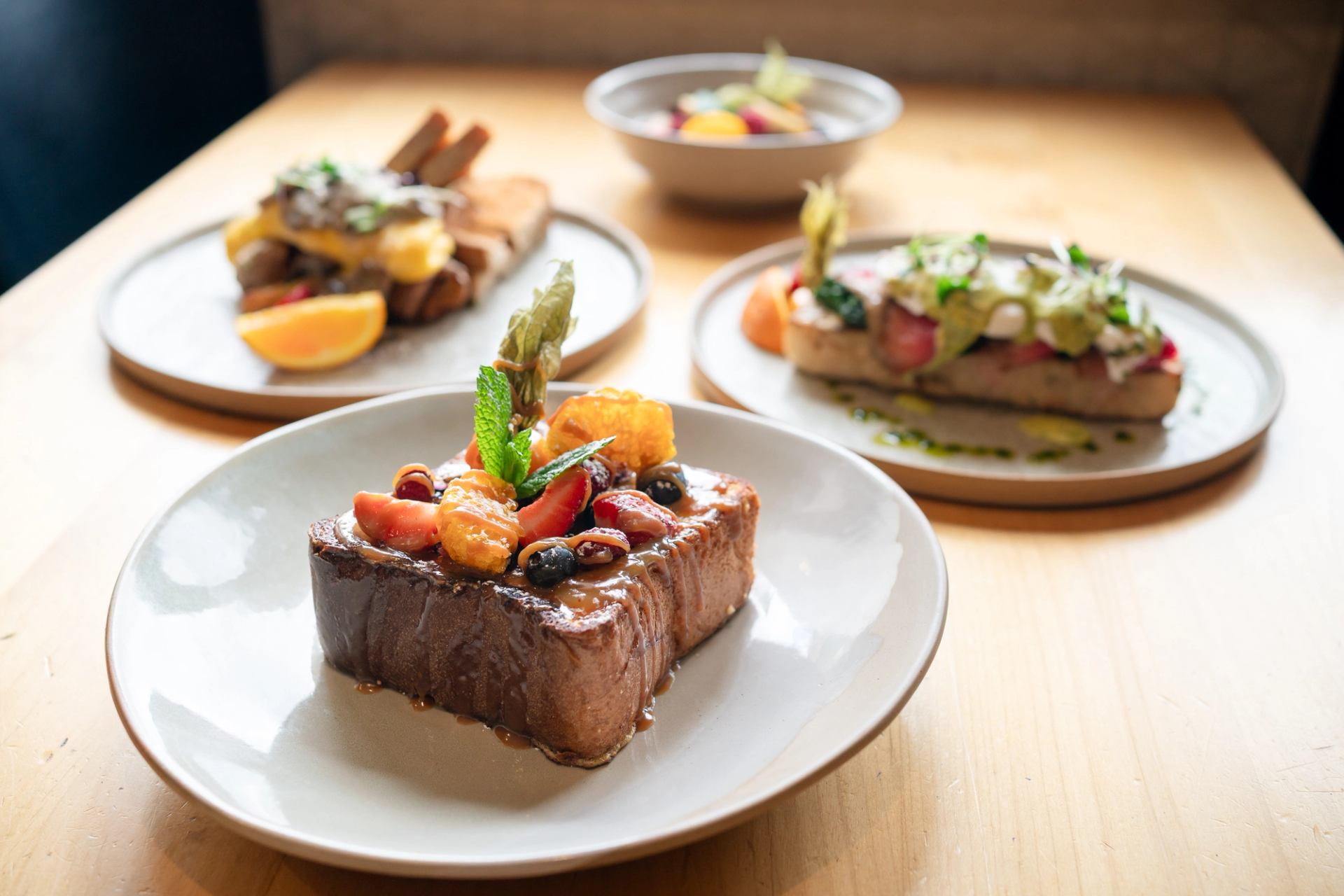 Creme Brulee French Toast with fresh fruit and miso caramel, other breakfast dishes in the back.