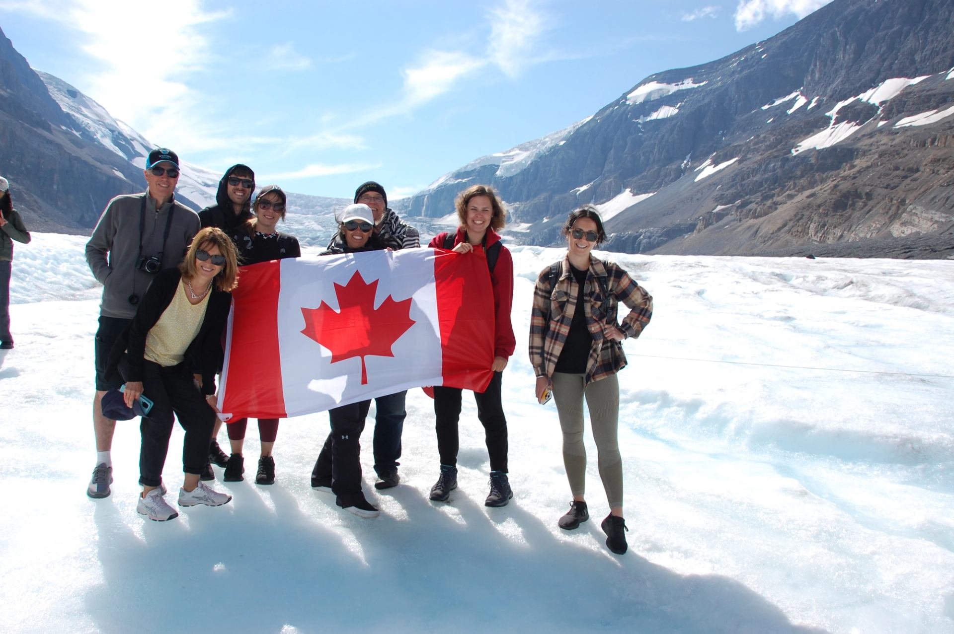 A group standing on a glacier holding a Canadian flag with mountains in the background.