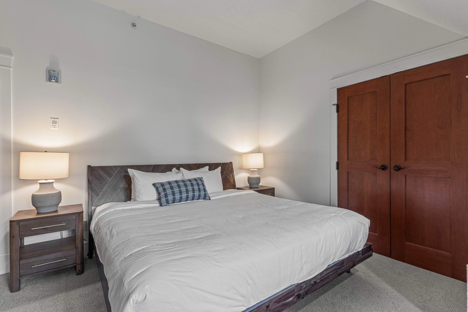 Bedroom with large bed, plaid cushion, two lamps, and wooden closet doors.