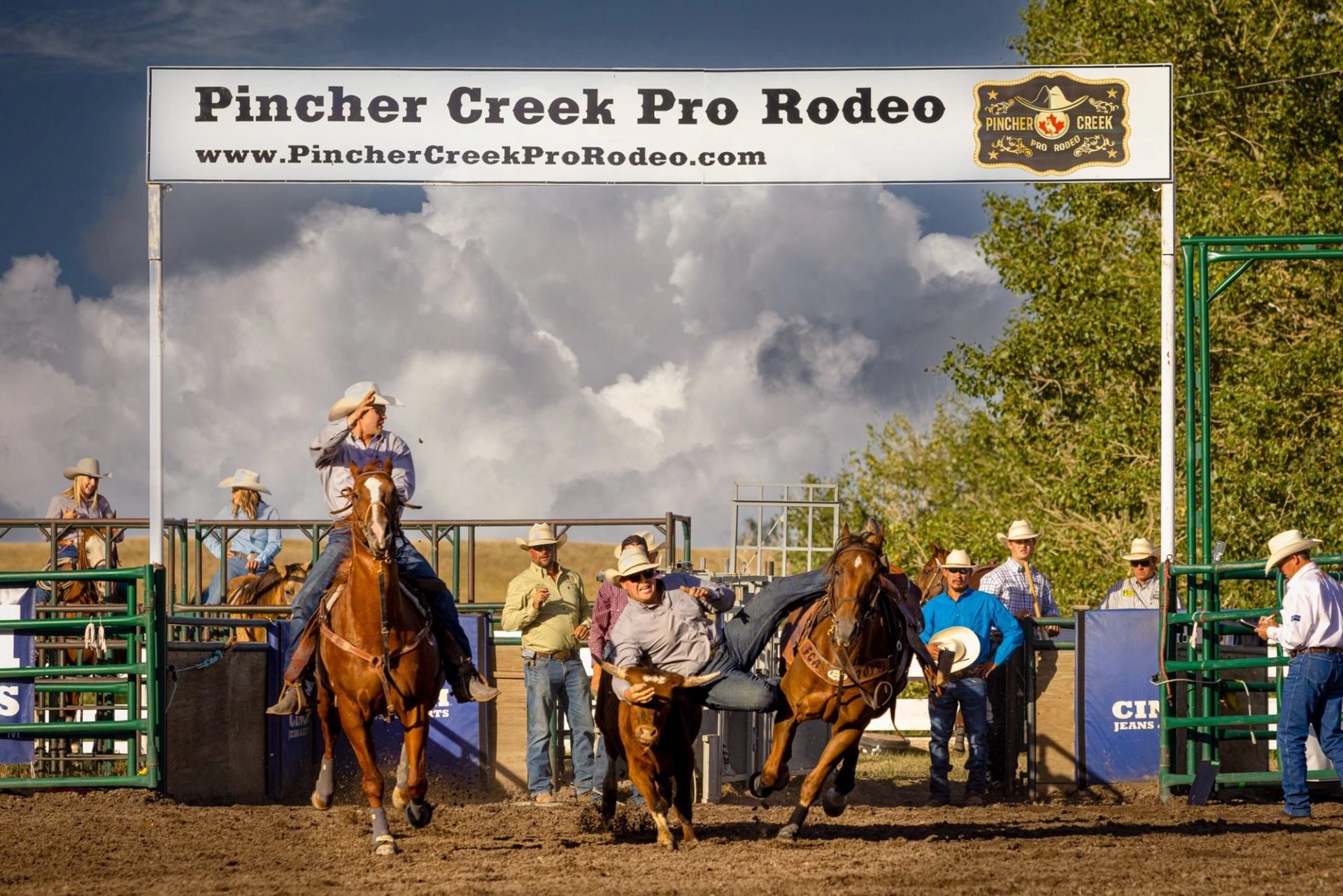Rodeo arena sign for Pincher Creek Pro Rodeo with mounted riders in the background.