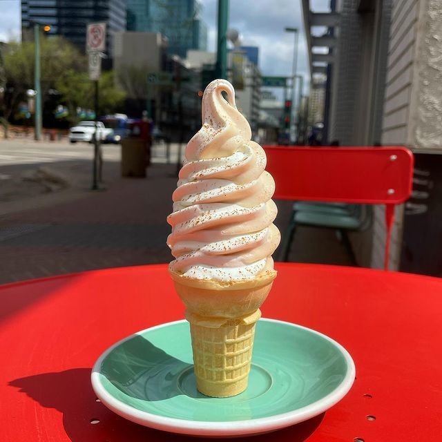 Vanilla soft‑serve cone standing on a green saucer on a red outdoor table.