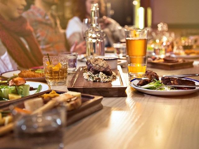 Table set with gourmet meals, drinks, and people enjoying dinner together in a warm setting.
