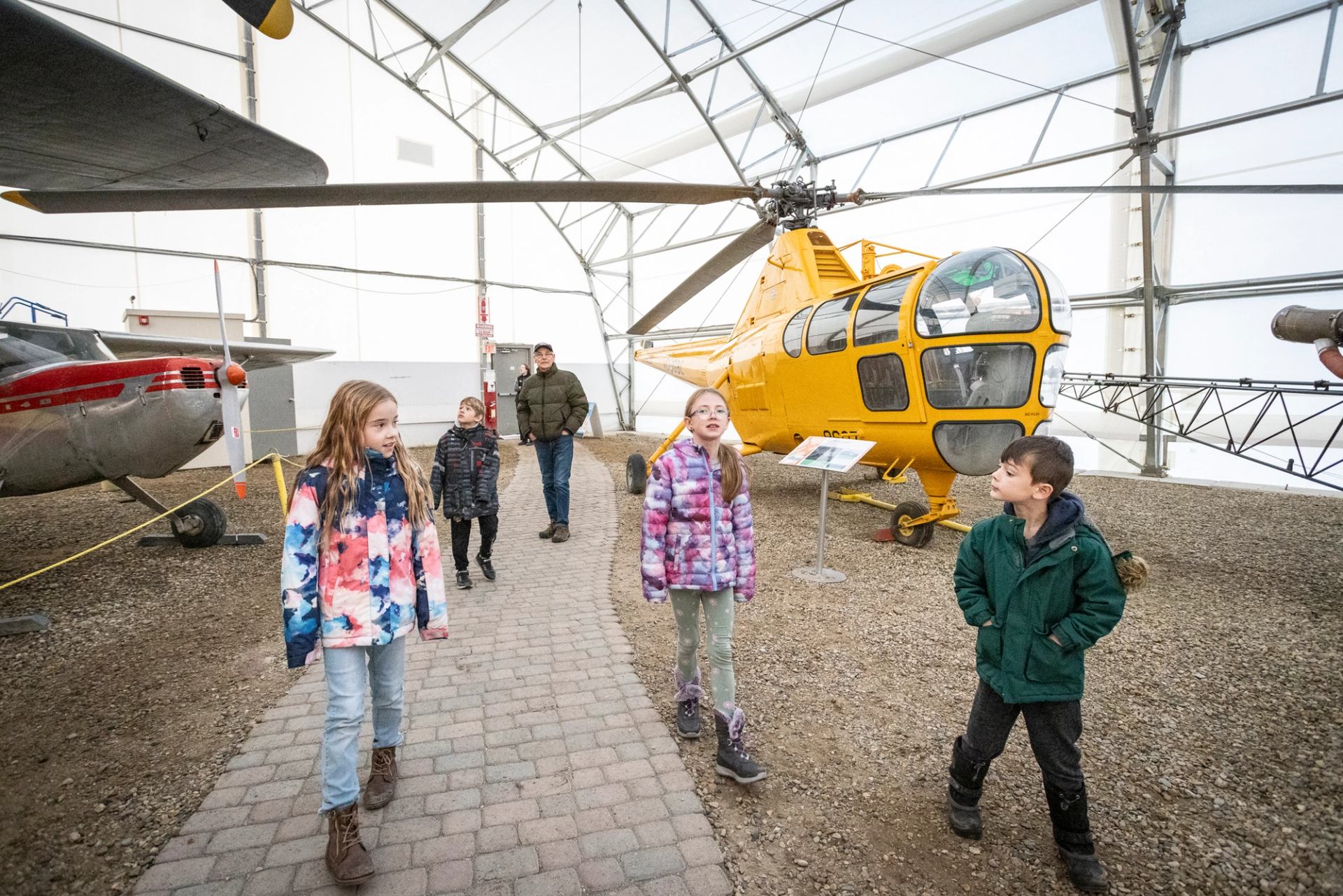 Yellow helicopter displayed inside museum hangar with three children walking nearby.