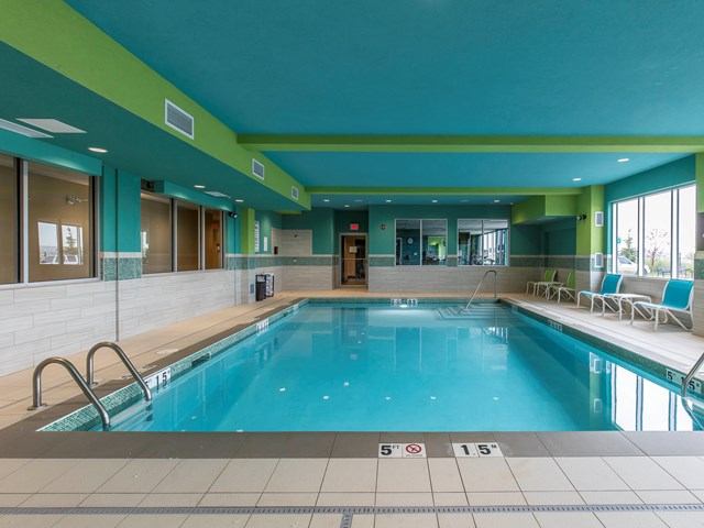 Indoor hotel pool with bright teal walls and seating along the side.
