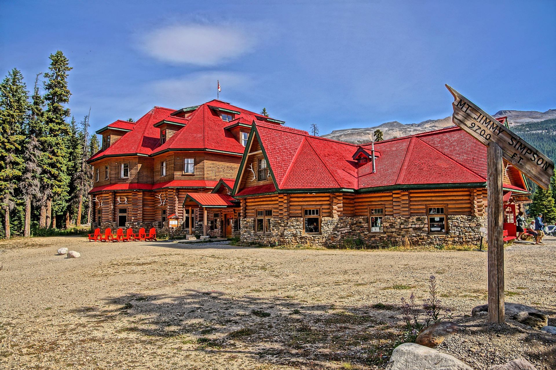 Large log lodge with red roofs, forest backdrop and Mt. Jimmy Simpson signpost.