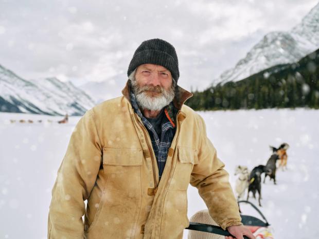 A portrait of the Dog Driver with his sled dogs in the background in Spray Lakes, Kananaskis.