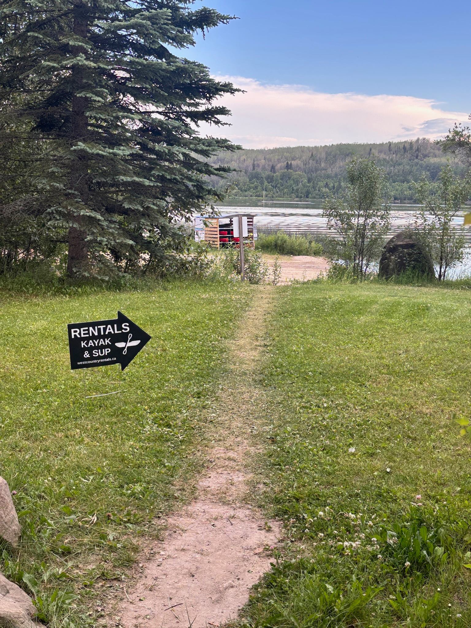 Kayak and SUP rentals sign beside grassy path leading to lake.