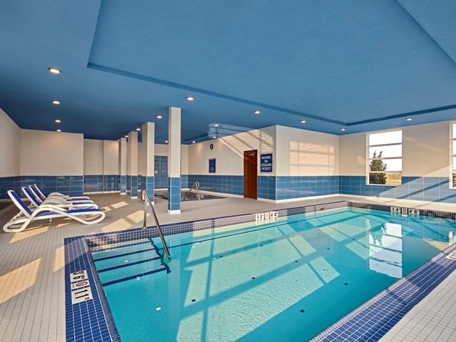 Indoor pool with lounge chairs and blue ceiling at Four Points Sherwood Park.