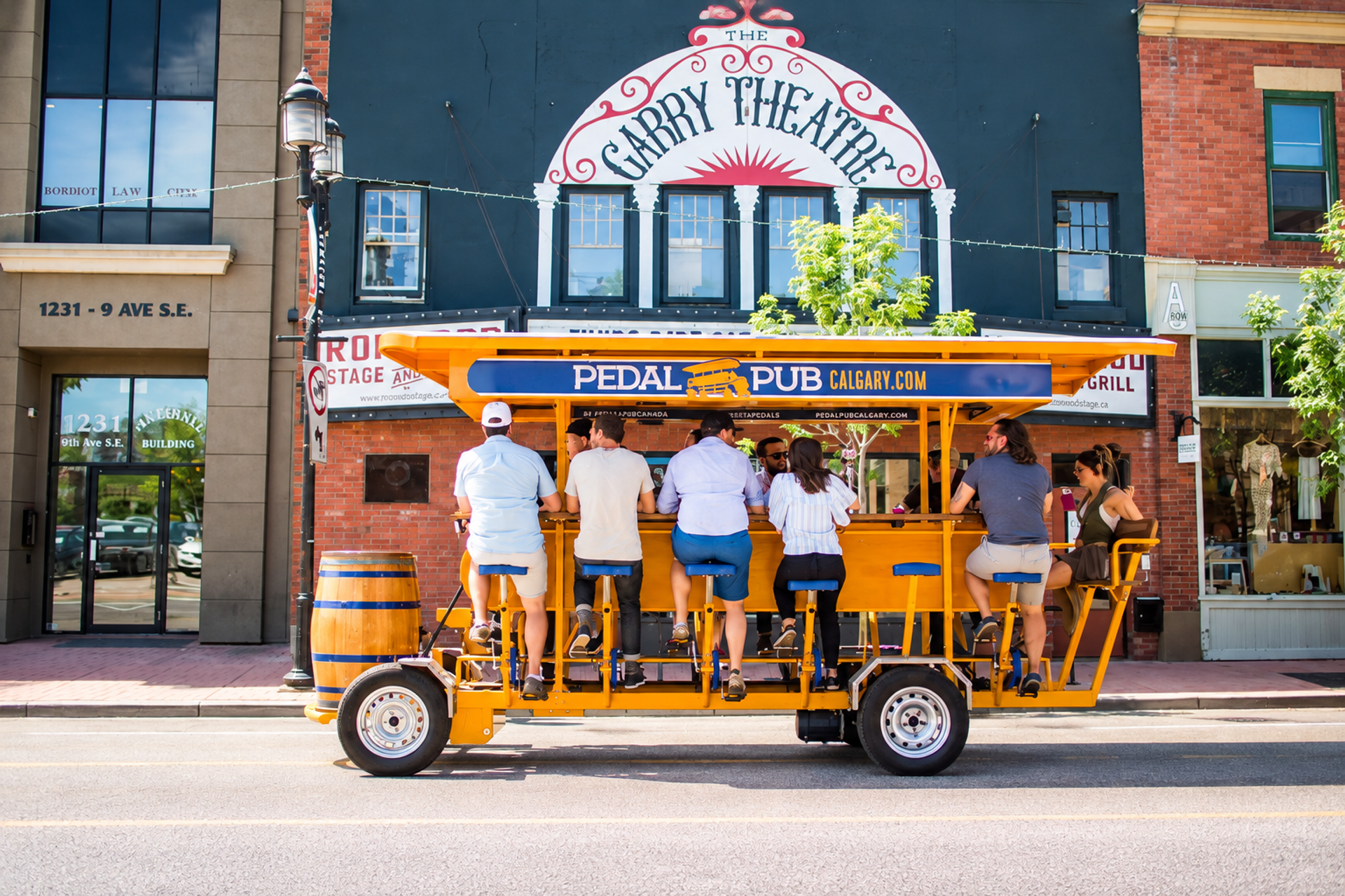 People ride an orange Pedal Pub past the Garry Theatre in Calgary.