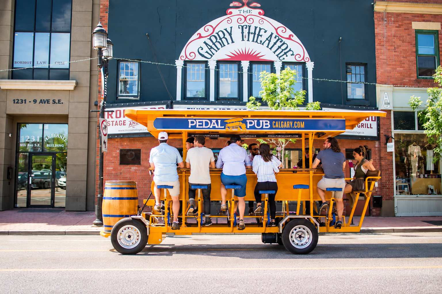 People ride an orange Pedal Pub past the Garry Theatre in Calgary.