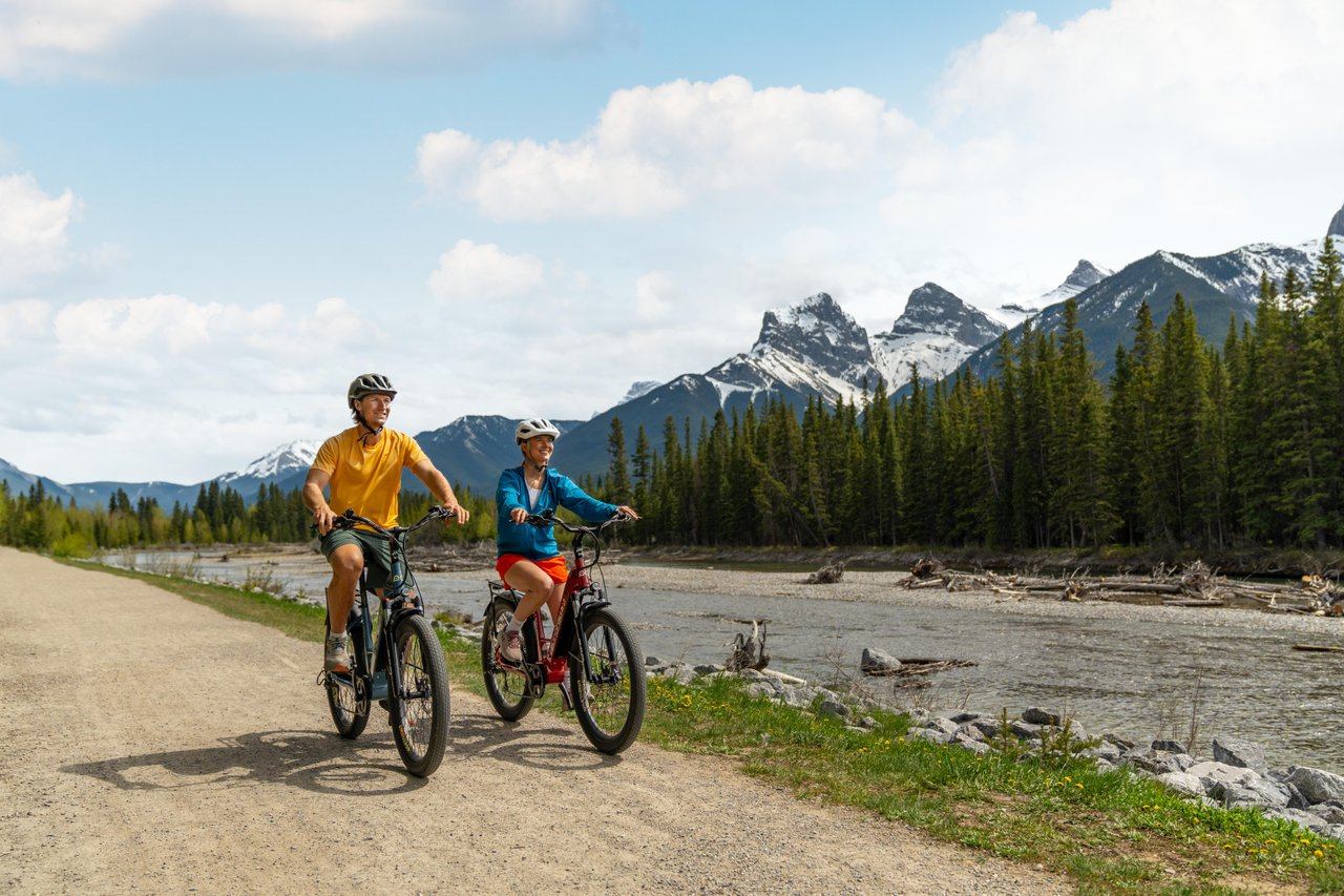 People biking along the Bow River with the Three Sisters Mountains in the background
