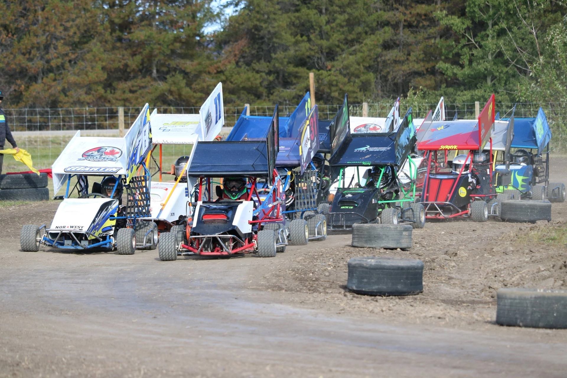 Cluster of mini sprint cars racing around a dirt track bordered by tires.